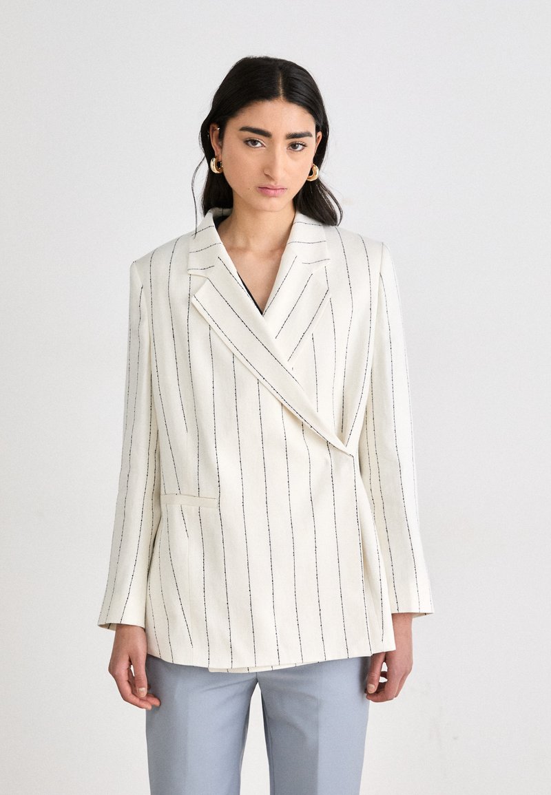 Blazer blanco con rayas verticales azules, diseño de doble botonadura, solapas con muesca y bolsillo frontal. Tejido suave, corte entallado.