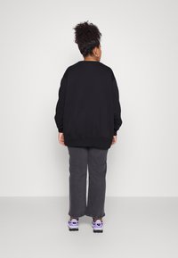 Črn oversize pulover z ribanim robom in manšetami, v kombinaciji s sivimi širokimi hlačami in supergami s vijoličnimi poudarki. Preprost, sproščen outfit.
