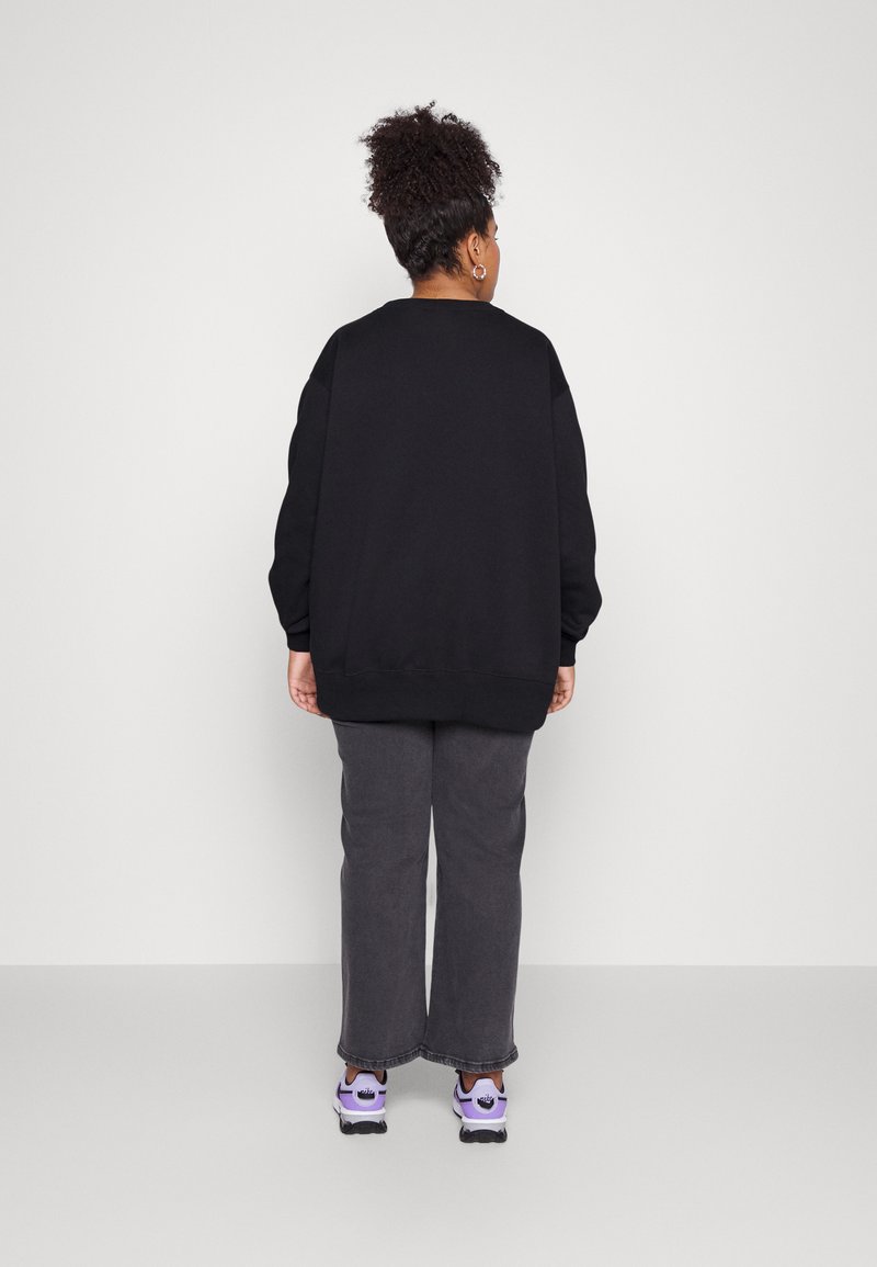 Svart oversized sweatshirt med ribbade manschetter och fåll, tillsammans med grå vida byxor och sneakers med lila detaljer. En enkel, avslappnad outfit.