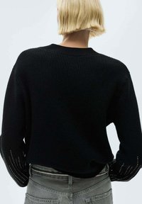 Schwarzer gestrickter Pullover mit Rundhalsausschnitt, der eine gerippte Textur und dekorative Lochstrickdetails an den Ärmeln aufweist.