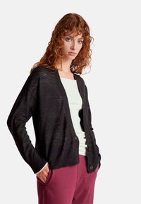 Černý cardigan vyrobený z měkkého úpletu, s volným střihem, dlouhými rukávy a dvěma předními knoflíky. Kombinujte s lehkým topem a vínovými kalhotami.