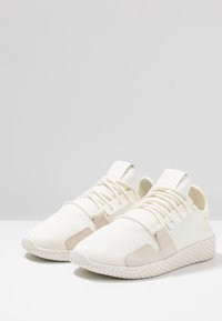 Vita tygskor med texturerad ovansida, tonade accenter, platta snörning och ett mönstrat sål. Minimalistisk design med rund tå.