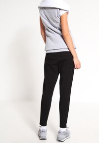 Un haut sans manches gris superposé sur un t-shirt blanc, associé à un pantalon slim noir et des chaussures de sport grises avec des accents blancs.