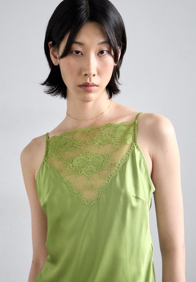Green silk camisole featuring a lace overlay with floral embroidery at the neckline. Spaghetti straps and smooth texture enhance its design.