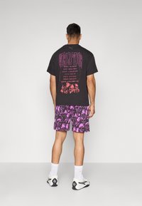 Sort t-shirt med pink "WORLD TOUR" grafik og kranie design på ryggen, parret med lilla shorts med kranie mønster.