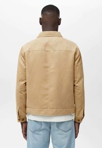 Light beige jacket with a smooth texture, a collar, and buttoned cuffs. Worn with light blue jeans, viewed from the back.