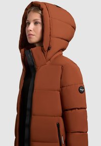 Chaqueta acolchada marrón con una gran capucha, con cremalleras negras, parche con logo en la manga y una textura suave. Diseño cálido e impermeable.
