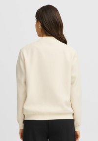 Cream-colored sweatshirt with a textured pattern, ribbed cuffs, and a round neckline. The back view shows a relaxed fit design.