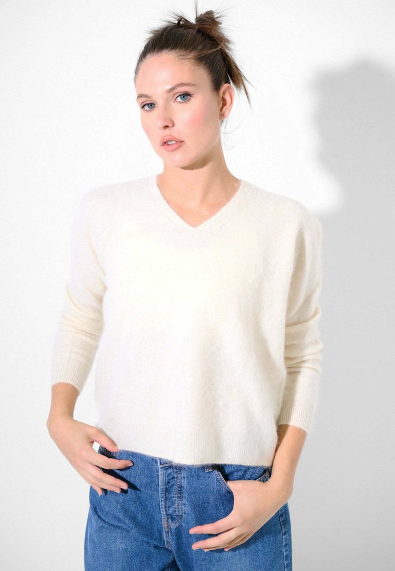 Maglione leggero color crema con scollo a V e maniche lunghe, dal tessuto morbido, abbinato a jeans in denim a vita alta.