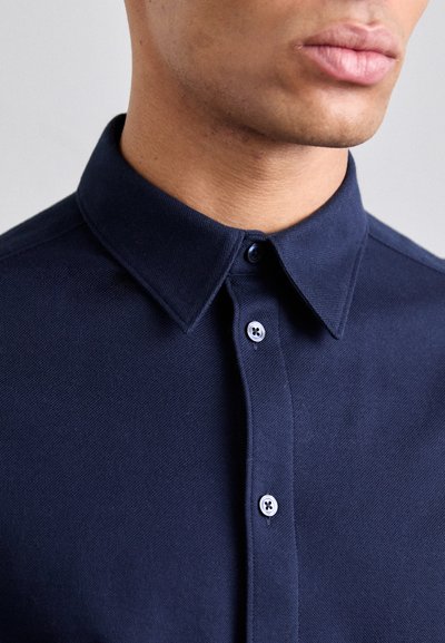 Polo navy de tejido texturizado, con cuello clásico y una tapeta de dos botones con botones en contraste. Vista en primer plano.
