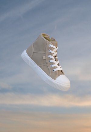 Sneaker beige alta con lacci bianchi e suola in gomma bianca che fluttua contro uno sfondo di cielo nuvoloso.
