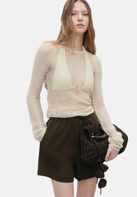 Lichtgewicht witte netten lange mouw top met een diepe V-hals, gecombineerd met donkerbruine shorts met trekkoord en een bruine geweven handtas met franjes.