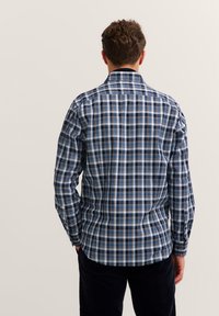 Camicia a quadri blu, bianca e nera. Dotata di maniche lunghe, colletto classico e vestibilità sagomata. Tessuto in cotone con una superficie liscia.