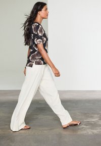 Floral-print black and cream short-sleeve top paired with wide-leg cream trousers and brown sandals, walking on a concrete floor.