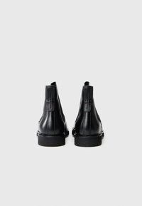 Botas de tobillo de cuero negro con una textura suave, paneles laterales elásticos y una suela de goma plana. Presenta un logotipo en la parte posterior.