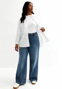 Vit skjorta över en vit t-shirt, kombinerat med högmidjade, vida blå denimjeans och vita skor. Enkel, avslappnad design.