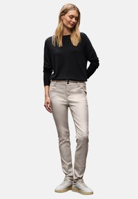 Jasne beżowe spodnie skinny z dwiema przednimi kieszeniami, zapięciem na dwa guziki i gładką fakturą. Połączone z czarnym swetrem z długim rękawem i białymi trampkami.