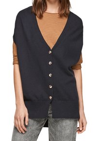 Mörkblå cardigan med djup V-ringning, knäppning med knappar, ribbat nederkant och oversized design, lagd över en brun skjorta.