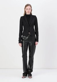 Black fitted blazer with long sleeves and single button closure, paired with high-waisted black leather pants and strappy black sandals.