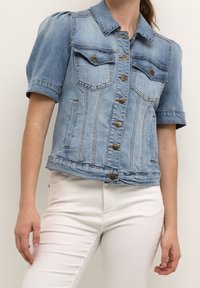 Giacca di jeans azzurro chiaro con maniche corte a sbuffo, tasche frontali e chiusure a bottoni in bronzo. Presenta una forma aderente e dettagli cuciti.