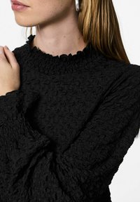 Crni dugih rukava teksturirani top s naboranim izrezom i elastičnim manšetama, s uzorkom naboranog tkanja. Približni prikaz detalja tkanine.