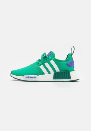 Baskets Adidas NMD vertes avec des rayures blanches, un talon violet et une semelle blanche coussinée sur un fond clair uni.