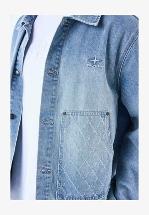 Light blue denim jacket featuring a quilted pocket, button details, and an embroidered logo on the chest. Smooth texture and casual fit.