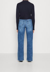 Blå denimbyxor med vida ben och en tvättad finish, femfickorsdesign och kontrasterande sömmar, kombinerat med en figurnära svart tröja.