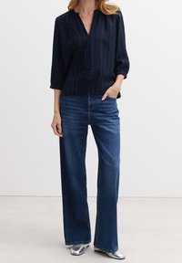 Camicia a righe navy con bottoni, scollatura a V e maniche a tre quarti, abbinata a jeans larghi blu scuro e scarpe argentate.