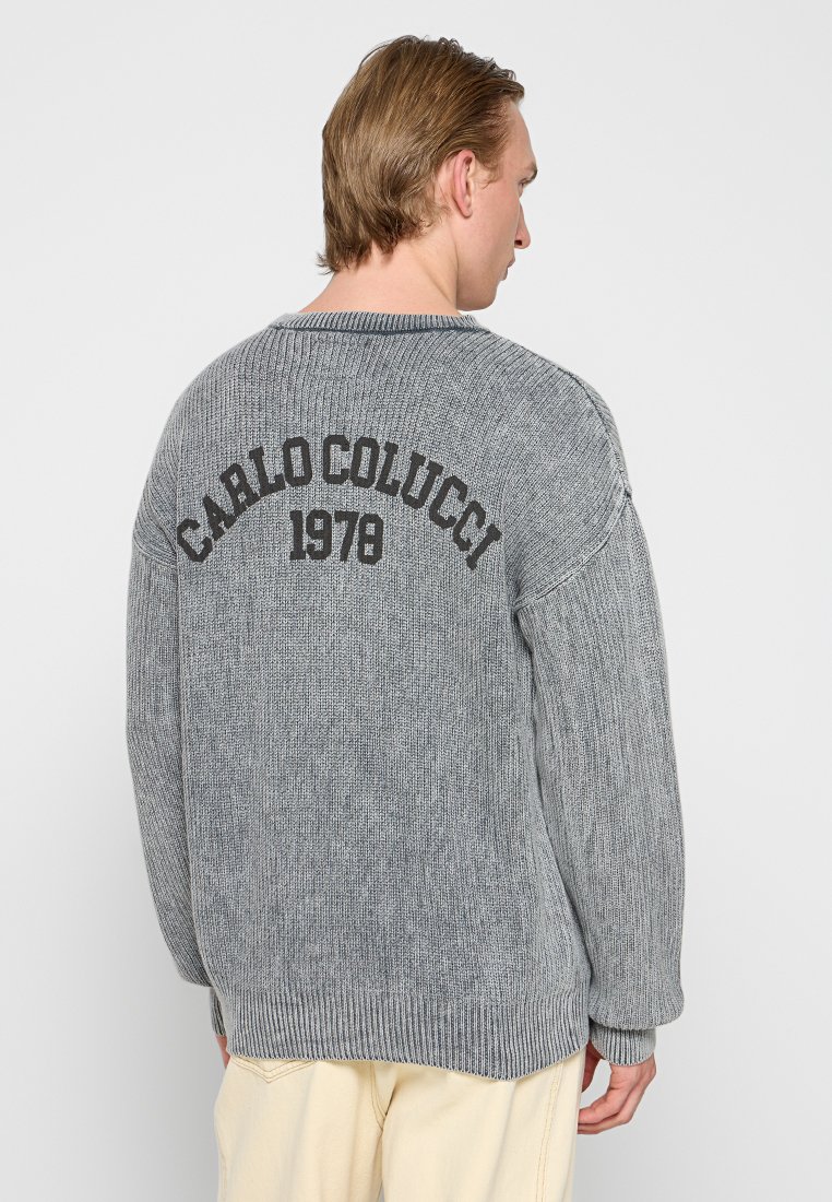Grijze gebreide trui met een losse fit, ribbelmanchetten en -zoom, met "CARLO COLUCCI 1978" in het zwart gedrukt op de achterkant.