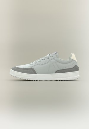 Jasnoszary sneaker z białą podeszwą, wykonany z materiałów skórzanych i zamszowych, z sznurowanym zapięciem, okrągłym noskiem oraz subtelnymi akcentami logo po bokach.