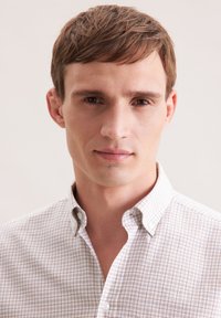 Una camicia button-down a quadri di colore chiaro presenta un colletto e motivi sottili con una texture morbida. Il tessuto appare traspirante e informale.