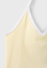 Débardeur jaune clair avec fines bretelles blanches et bordure blanche le long de l'encolure et des emmanchures sur fond uni.