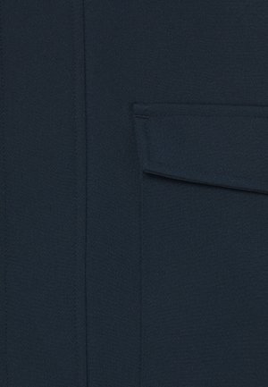 Ciemnod granatowy materiał z prostokątną kieszenią z klapą, posiadającą przeszywane krawędzie i pionowy detal szwu po lewej stronie.