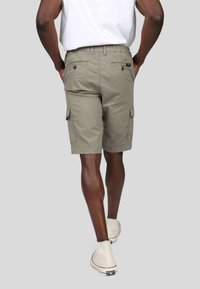 Shorts cargo en khaki clair, faits en tissu durable, avec des poches latérales et une coupe décontractée, associés à des chaussures crème.
