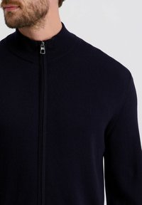 Marineblaues Zip-Up-Pullover mit hohem Kragen und gerippter Textur, ausgestattet mit einem Metallreißverschluss und tailliertem Schnitt. Dünnes und leichtes Material.