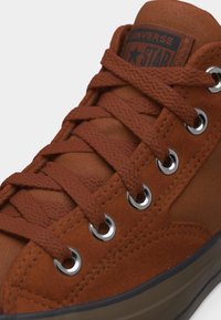 Krupan plan Converse tenisice boje hrđe s teksturiranim vezicama, metalnim otvoračima za vezice i vidljivim logotipom "Converse All Star" na jeziku.