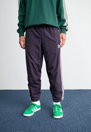 Paarse sportbroeken met witte zijstrepen, elastische tailleband en logo. Gecombineerd met groene sneakers met witte strepen en zool.