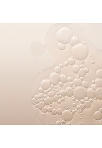 Klar vätska med många bubblor i olika storlekar som reflekterar ljus, mot en mjuk beige bakgrund. Slät textur, glänsande yta.