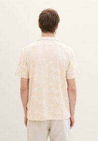 Kortärmad krämfärgad skjorta med ett diskret palmbladsmönster, kragsdesign och mjuk textur; bärs med ljusfärgade byxor.