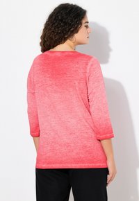 Camicia rossa, ombre, a tre quarti con una texture morbida e un collo rotondo. Il colore passa da un rosso scuro a un rosso chiaro.