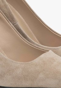 Beige suede hoge hakken met een ronde neus en een gladde binnenvoering. De textuur is zacht met een matte afwerking en heeft minimale stiksels.