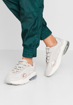 Helle graue Sneaker mit strukturierter Oberseite, Schnürdesign und durchsichtiger Luftpolsterung in der Sohle. Akzente sind dezente roségoldene Details.