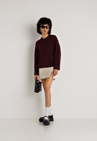 Bordo pleteni pulover, krema mini krilo s stranskim razporkom, črne platforme, bele nogavice, črna torbica s pikami, sončna očala, teksturirani lasje.