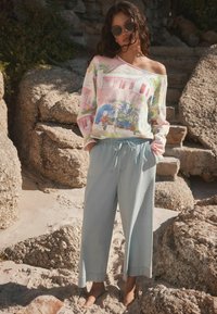 Kolorowy, bluzowy sweter typu off-shoulder z akwarelowym nadrukiem architektonicznym, w zestawieniu z jasnoniebieskimi, szerokimi spodniami lnianymi z elastyczną talią.