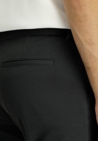 Zwarte broeken van een gestructureerde stof, met een enkele achterzak en een slank, taps toelopend ontwerp, dat gedeeltelijk zichtbaar is bij de taille.