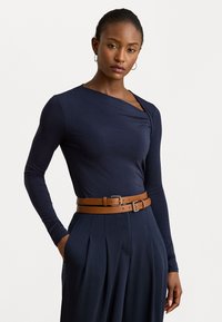Marineblauwe top met lange mouwen en een gedrapeerde halslijn, gecombineerd met hooggewaisted geplooide broeken en een bruin leren riem met dubbele gesp.
