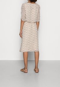 Lichtgewicht, gemêleerde jurk met korte mouwen, een getailleerde taille en een knielange rok in beige met bruine bloemenaccenten. Bruine sandalen.