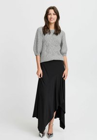 Grauer Strickpullover mit einem strukturierten Muster, kombiniert mit einem schwarzen asymmetrischen Rock. Das Model trägt silberne High Heels.