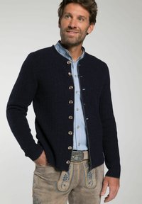 Donkerblauwe gebreide cardigan met een geribbelde textuur, voorzien van zilveren knopen en een rond decolleté, gedragen over een lichtblauw shirt en grijze broek.